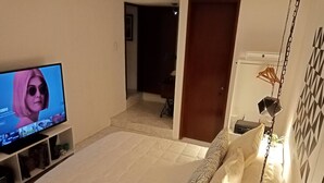 Ein Schlafzimmer mit einem Bett, einem Fernseher auf einem Schrank, einer Tür und einem kleinen Regal mit Gegenständen.