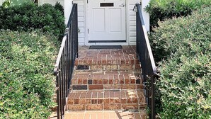 A white house with a front door, a brick staircase, and a letter "D" on the wall.