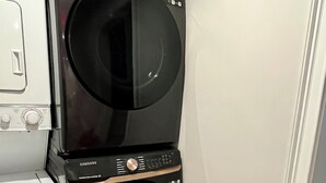A stacked washer and dryer unit in a corner with a wooden floor.