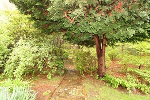 Stroll along the garden pathway to a shaded seating area under a large tree.