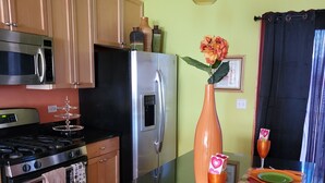 Une cuisine moderne dotée d’appareils électroménagers en acier inoxydable, d’un îlot central et d’un coin repas agrémenté d’assiettes colorées et d’un vase de fleurs.