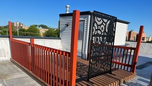 Un toit surmonté d’une clôture en métal rouge, un petit bâtiment blanc et une porte noire décorative.