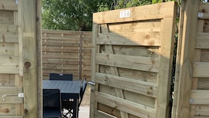A wooden gate with a number plate, leading to an outdoor seating area with a table and chairs. - La Voile Grise des Dunes (Koksijde)