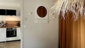 A bedroom with a bed, a hanging light fixture, a circular mirror, and a view of a kitchen. - La Voile Grise des Dunes (Koksijde)