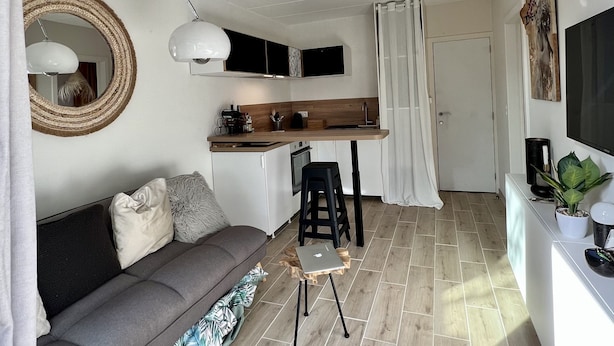 A compact living space with a kitchenette, a sofa, a dining area, and a TV. - La Voile Grise des Dunes (Koksijde)