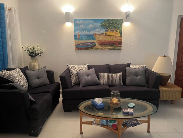 Un salon avec deux canapés, une table basse en verre et un tableau représentant un bateau accroché au mur.