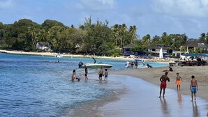 A beach with clear blue water, people walking along the shore, and a boat in the water.