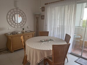 Un coin repas avec une table ronde, des chaises en osier, un miroir décoratif et une vue à travers une porte vitrée.