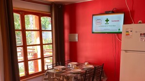 A dining area with a table set for four, a television mounted on the wall, and a refrigerator. - Parcela Los Nonos (Vicuña)