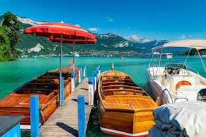A wooden pier with boats docked, a red umbrella, and a mountainous backdrop. - Home Sweet Home (Annecy)