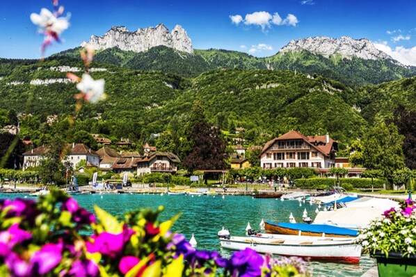 Un hotel frente al lago con barcos amarrados, rodeado de exuberante vegetación y montañas.