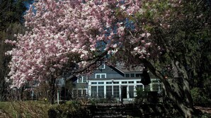 A house with a covered porch, a stone staircase, and a garden with blooming pink flowers. - Buttermilk Falls Inn (Milton)