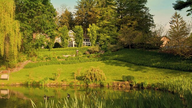 A serene garden with a pond, lush greenery, and a house in the background. - Buttermilk Falls Inn (Milton)