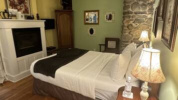 Un dormitorio con una cama, una mesita de noche con lámpara, chimenea y pared de piedra.