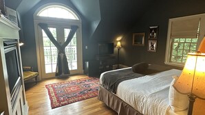 A bedroom with a large bed, a desk with a lamp, a TV, and a fireplace. - Buttermilk Falls Inn (Milton)
