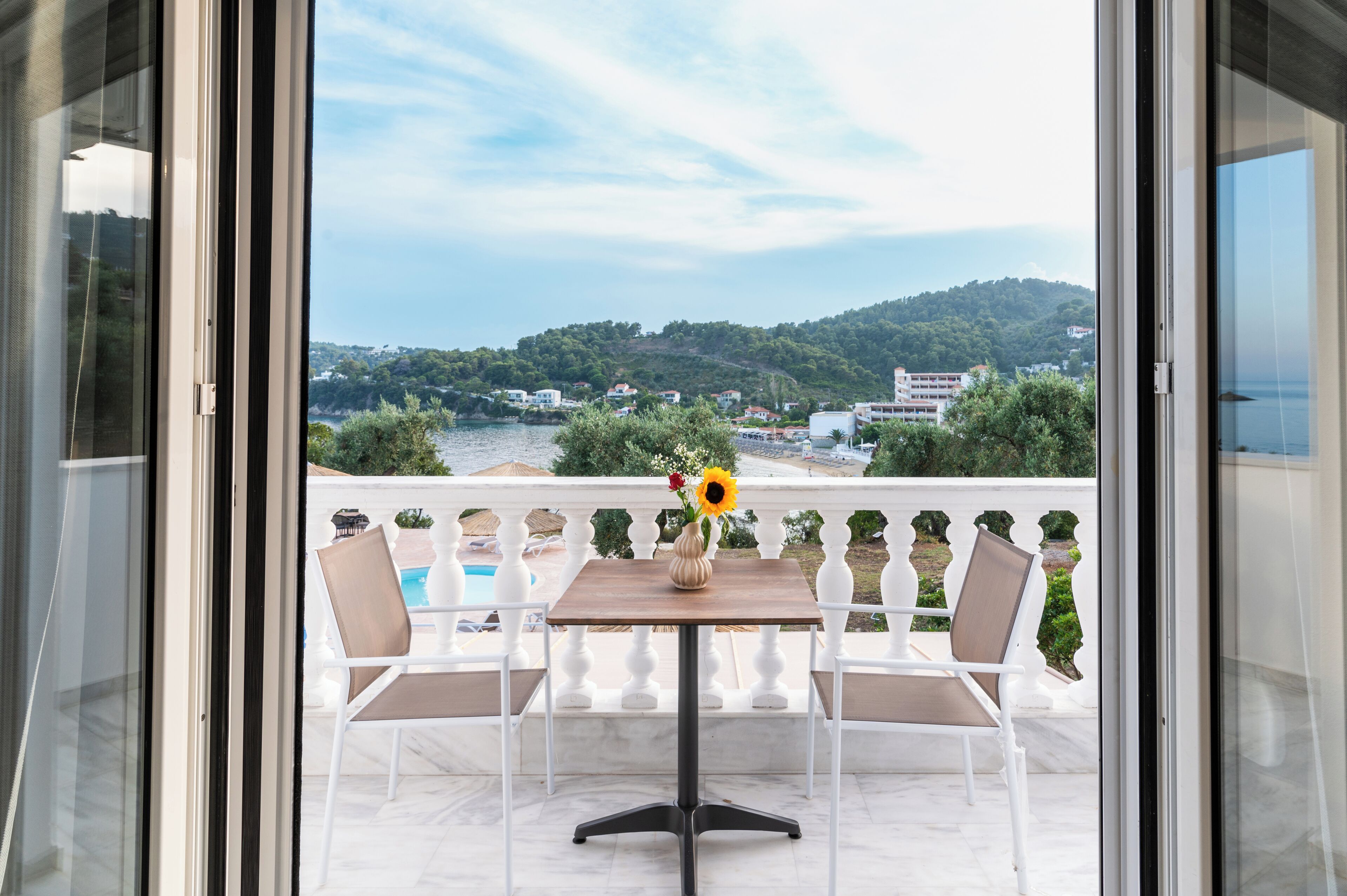 Un balcon avec une table et des chaises, un vase rempli de fleurs et une vue sur une piscine et des collines.