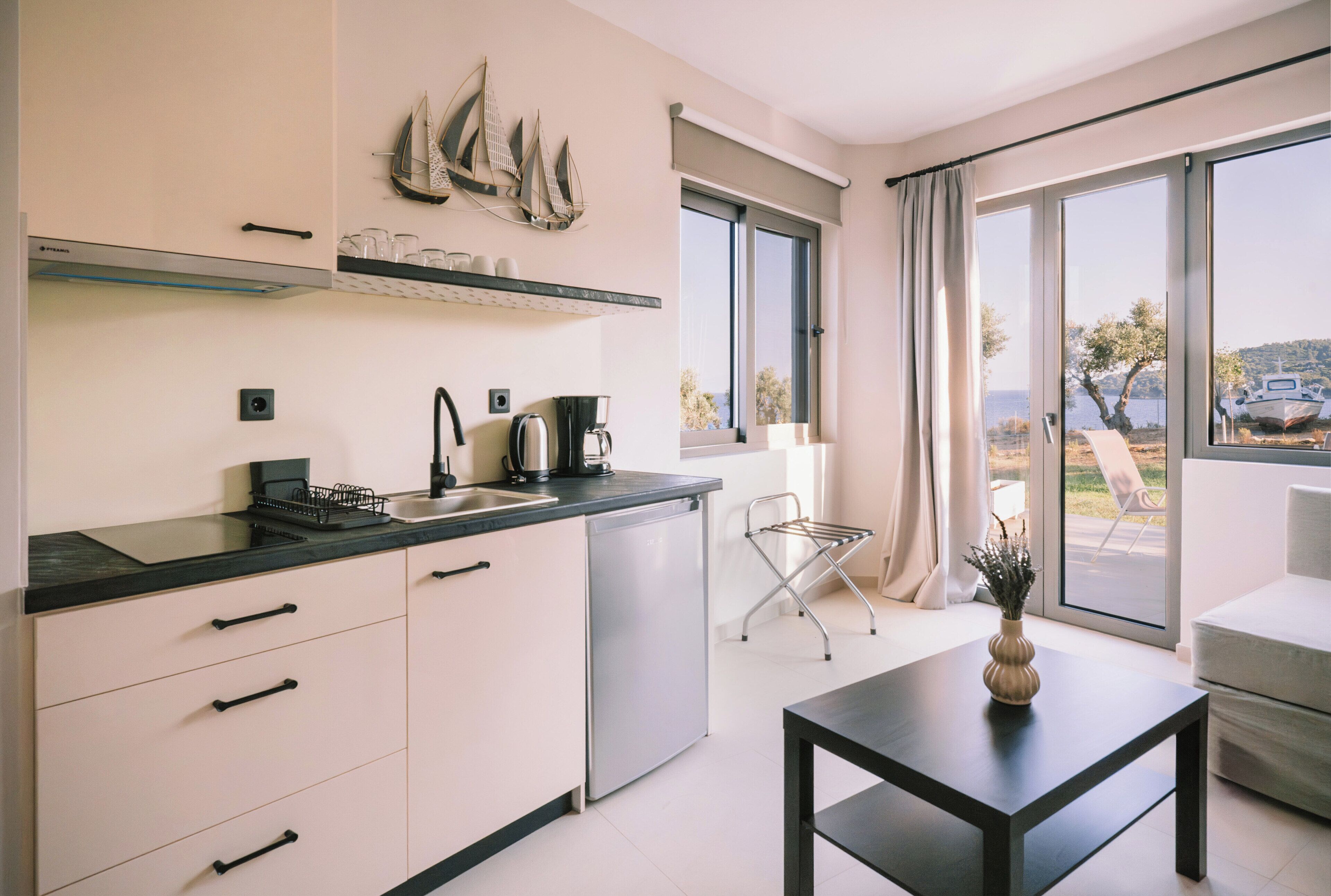A modern kitchen with a dishwasher, a coffee maker, and a window with a view of the sea.