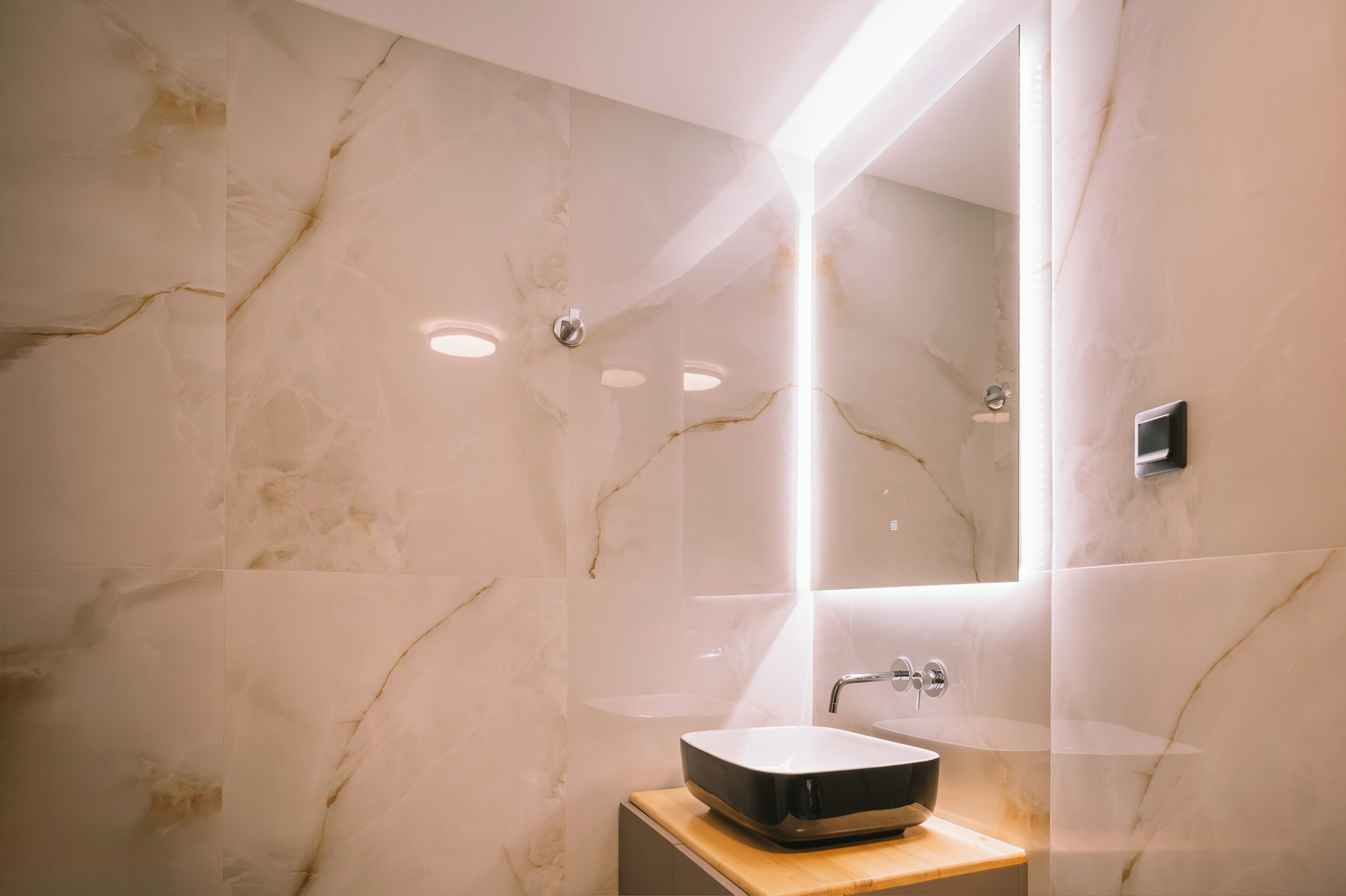 A modern bathroom with a marble wall, a vessel sink, and a large mirror.