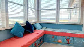 Una stanza con una panca integrata lungo una finestra, con un cuscino rosso e cuscini blu.