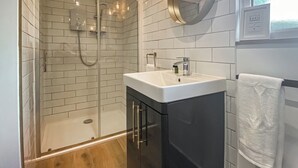 A modern bathroom with a glass-enclosed shower, a white sink with a mirror, and a towel hanging on a rack. - 1 bedroom accommodation in Hoxne, near Eye (Hoxne, near Eye)