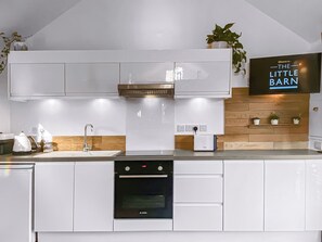 A modern kitchen with white cabinetry, a Bosch oven, a built-in microwave, and a television displaying 'The Little Barn' sign. - 1 bedroom accommodation in Hoxne, near Eye (Hoxne, near Eye)