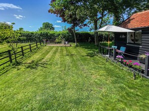 A well-maintained grassy yard with a wooden fence, a bench, and a small structure with a roof. - 1 bedroom accommodation in Hoxne, near Eye (Hoxne, near Eye)