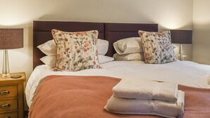 Un lit bien fait, agrémenté d’oreillers à motifs floraux, d’un plaid marron et d’une table de chevet avec une lampe.