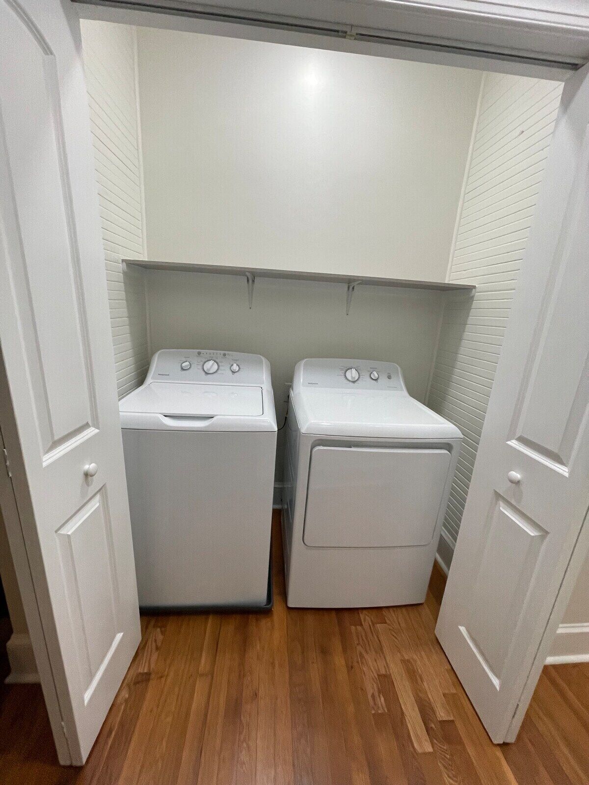 A laundry room with two white front-loading washing machines and a wooden floor.