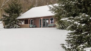 A wooden cabin with a snow-covered roof, surrounded by evergreen trees and a snow-covered ground. - Heron Hill at Secluded Cabins (Lakeville)