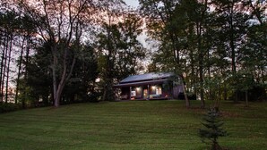 A cabin with a porch, surrounded by trees and a grassy area. - Dove Cottage at Secluded Cabins (Lakeville)