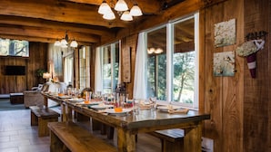 A wooden dining area with a long table set for a meal, benches, and large windows with natural light.
