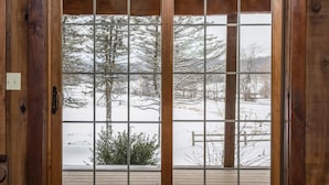 A wooden door with a glass panel, leading to a snowy outdoor area with a wooden deck and a bench.