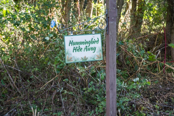 A sign with the text 'Hummingbird Hide Away' in a natural setting. - Hummingbird Hideaway (Lakeville)