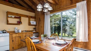 Una cocina de madera con una mesa de comedor para cuatro personas, un microondas y un gran ventanal con cortinas.
