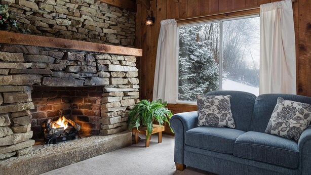 Una habitación acogedora con chimenea de piedra, un sofá azul y una ventana con cortinas.