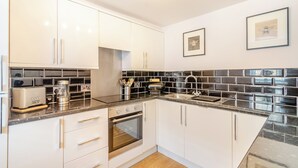 Una cocina moderna con armarios blancos, salpicadero de baldosas negras, electrodomésticos de acero inoxidable y un cuadro en la pared.