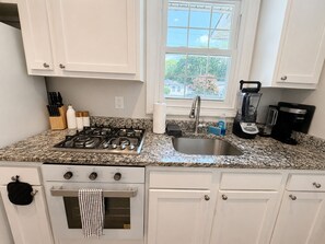 A kitchen with white cabinets, a gas stove, a sink, and a window with a view of greenery. - 6BR Crew Stay - Kitchen - Parking - Near I-26 - C (North Charleston)