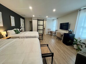 Une chambre d’hôtel avec deux lits, un bureau avec une télévision, une chaise et une petite table.