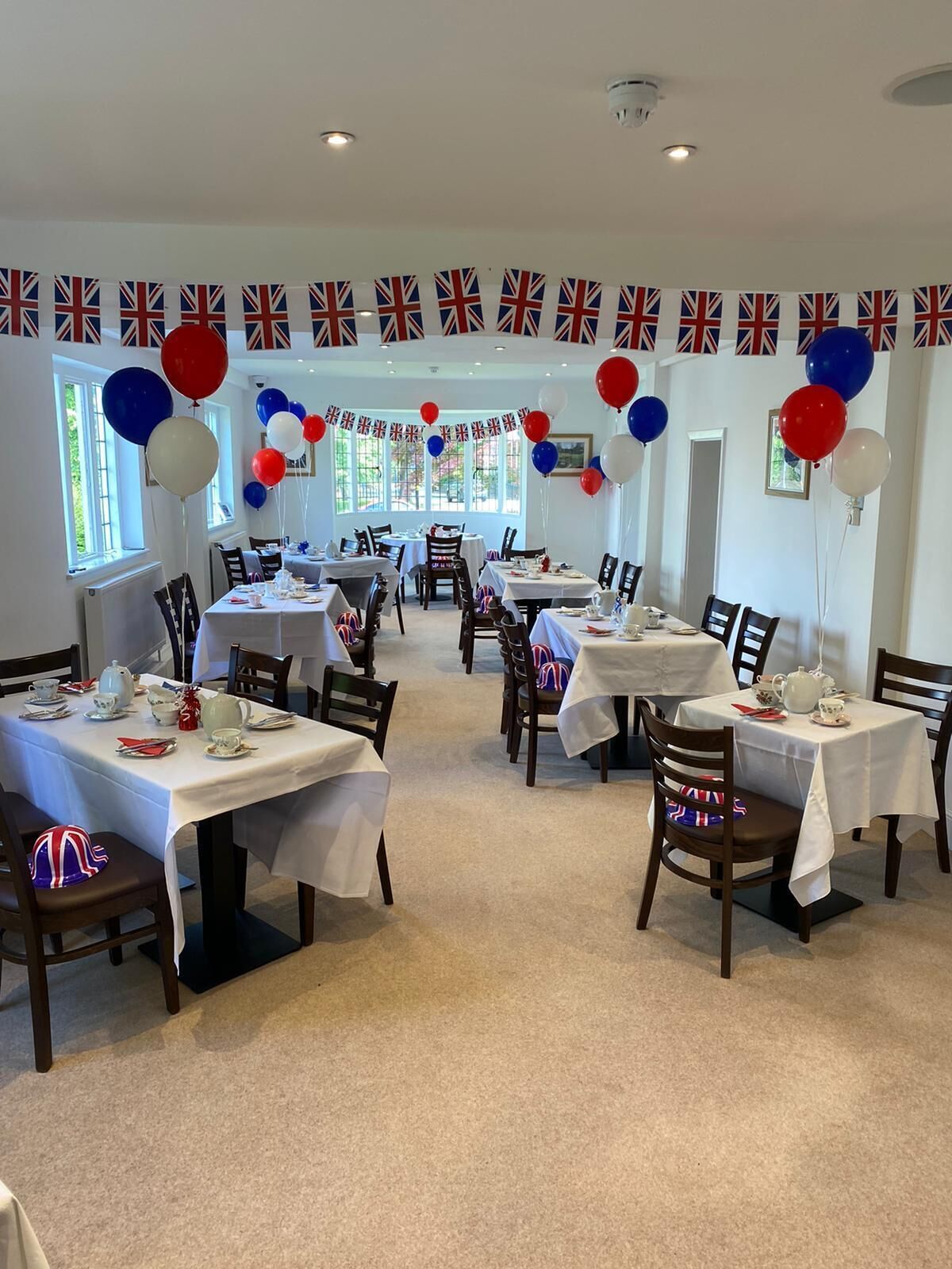 A dining area with tables set for a meal, decorated with British flags and balloons.