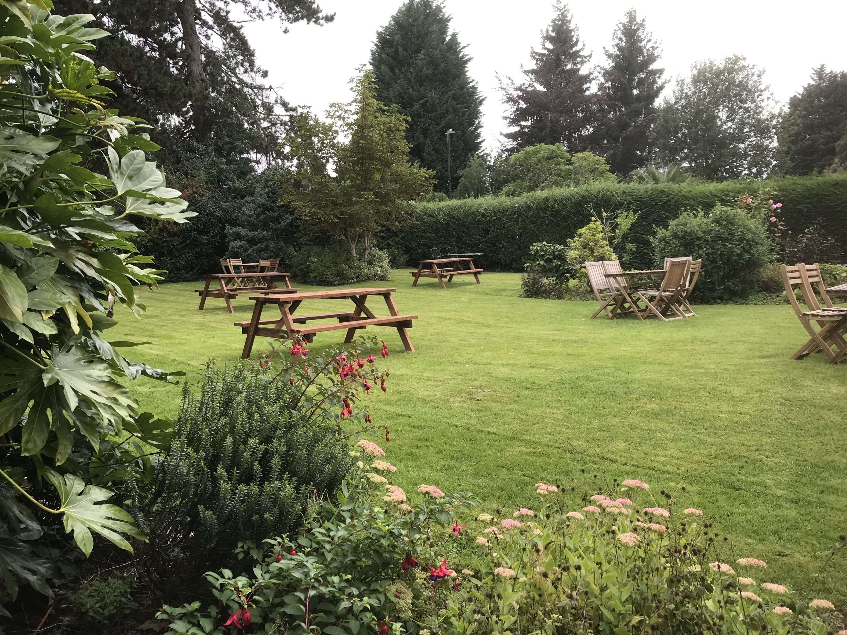 Un jardin bien entretenu, agrémenté de tables et de chaises pour pique-niquer, et entouré d’une végétation luxuriante et d’arbres.