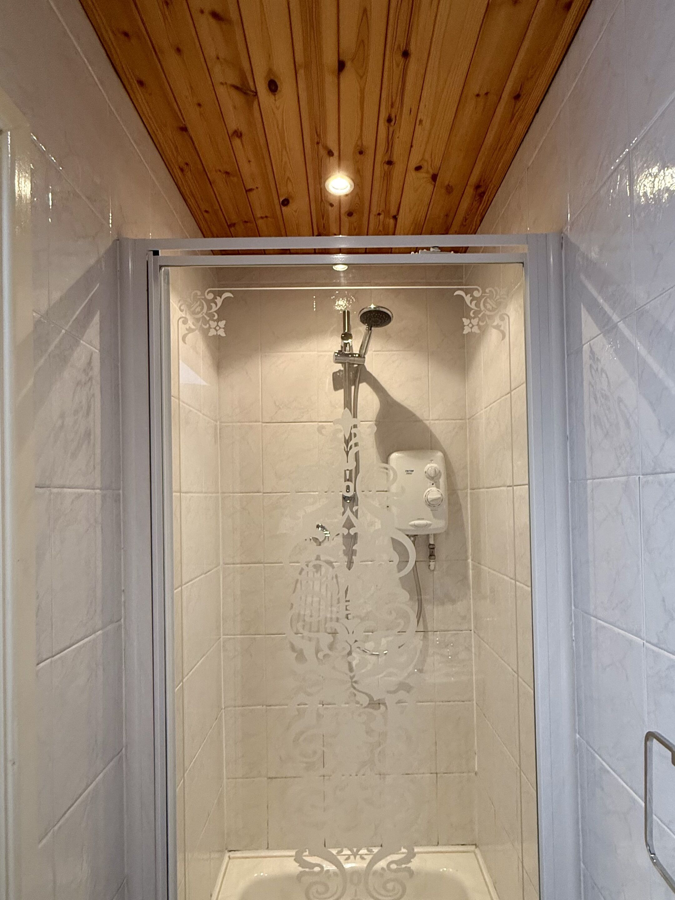 Un espace de douche doté d’un plafond en bois, de murs carrelés et d’un pommeau de douche.