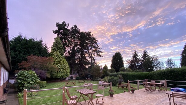 A wooden deck with outdoor furniture, surrounded by a well-maintained lawn and trees, under a twilight sky. - The Old Farm Hotel (Birmingham)