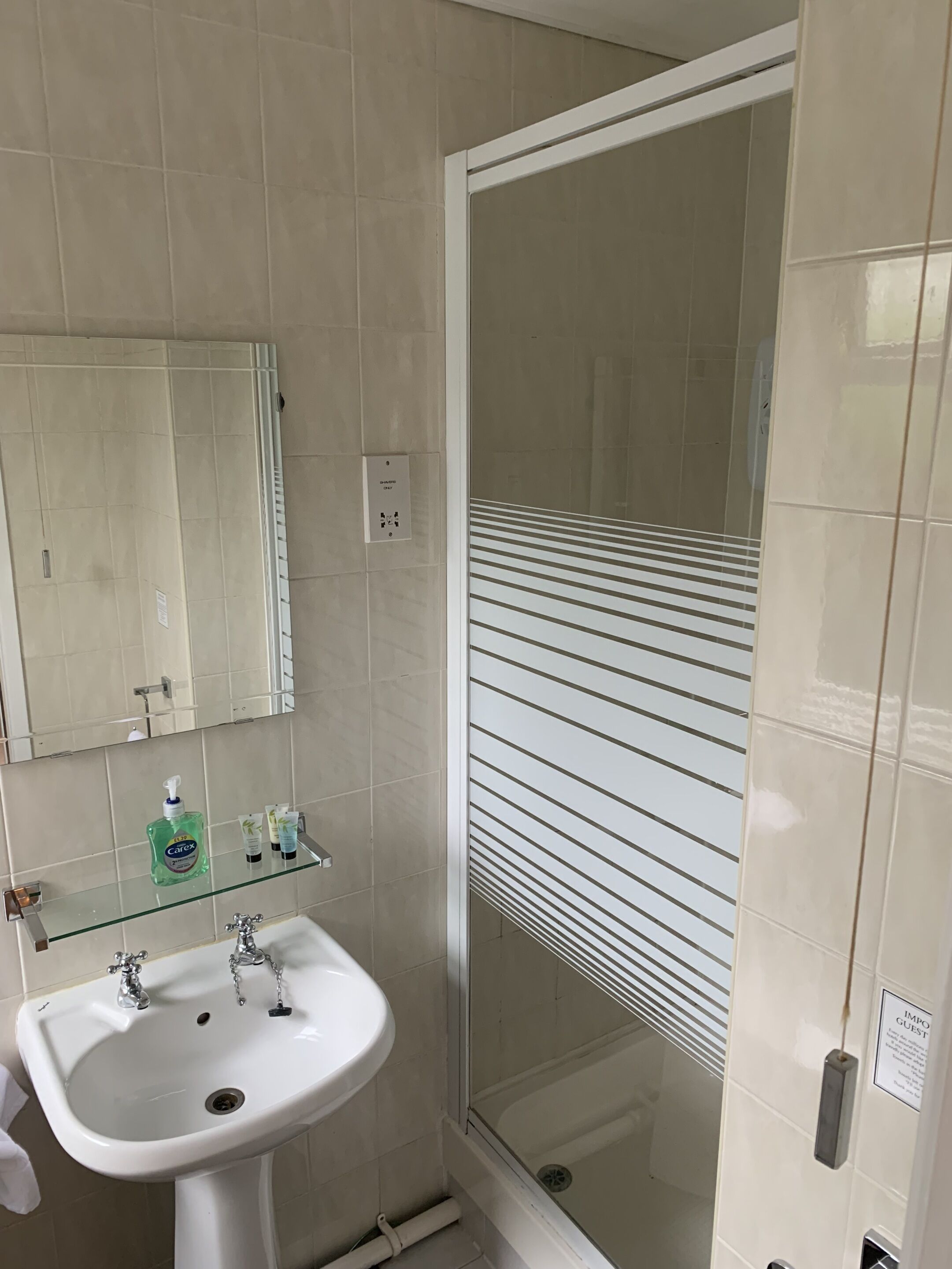 Une salle de bain avec un lavabo blanc, un miroir et une cabine de douche en verre.