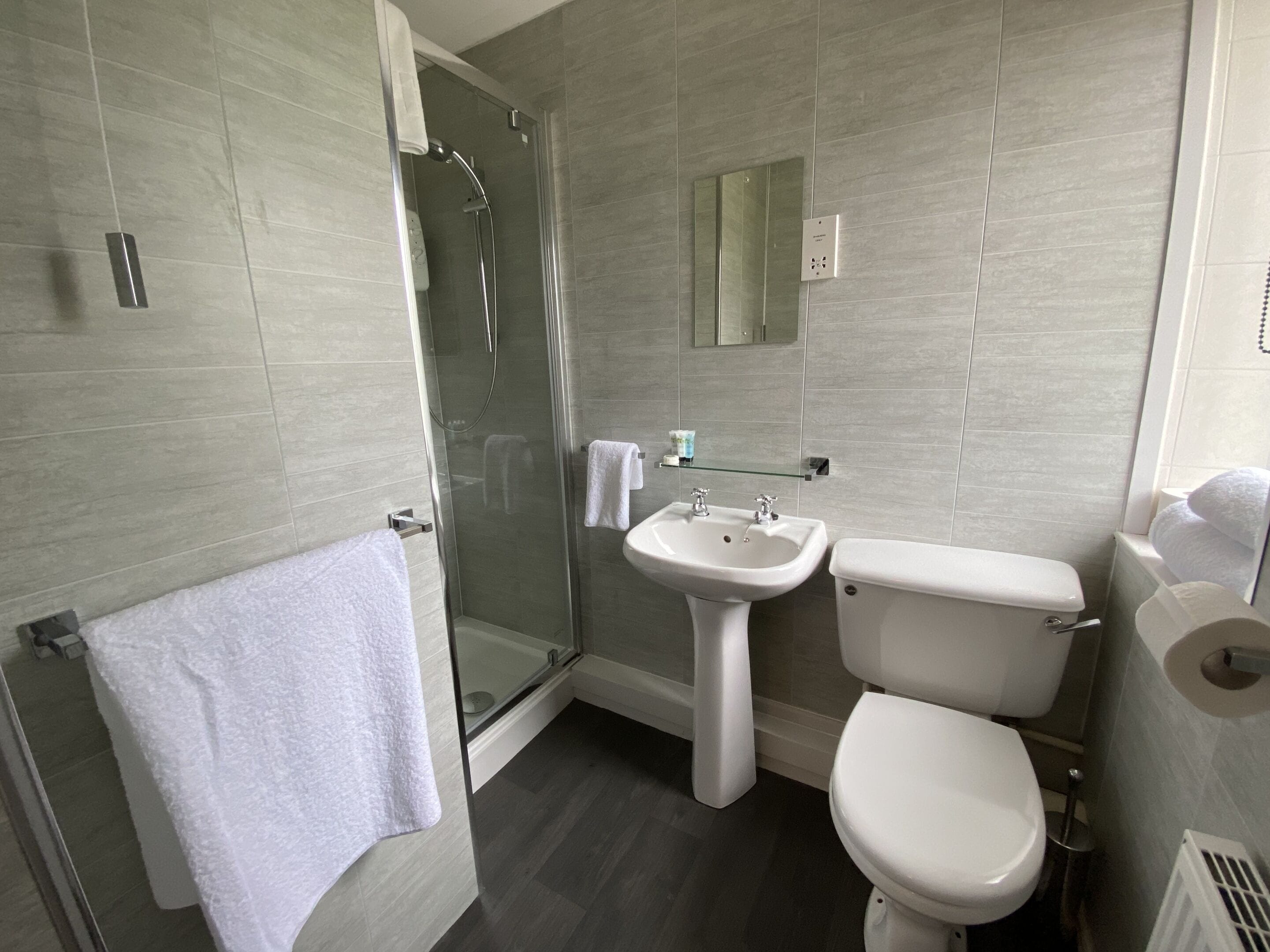 A modern bathroom with a glass shower enclosure, a pedestal sink, and a toilet.