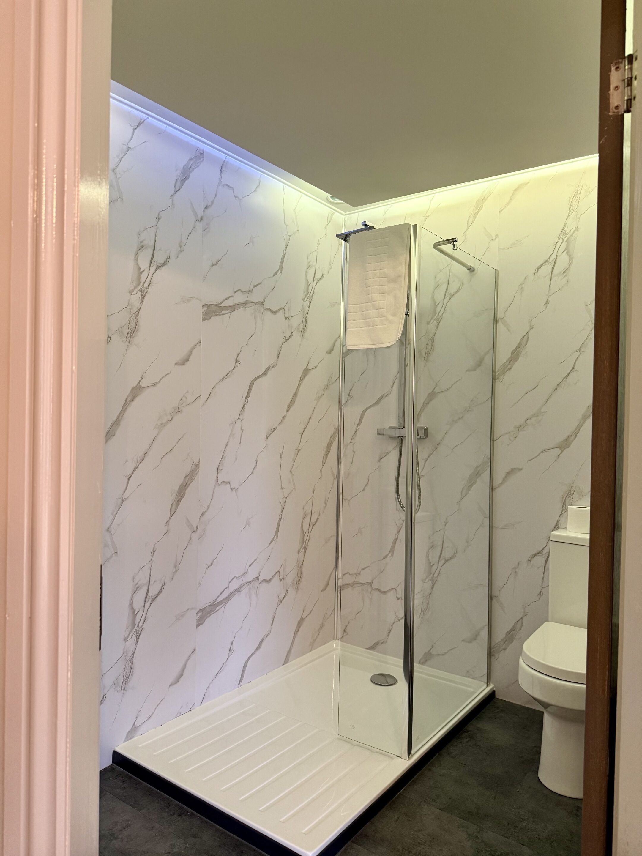 A modern bathroom with a glass-enclosed shower, marble walls, and a white toilet.