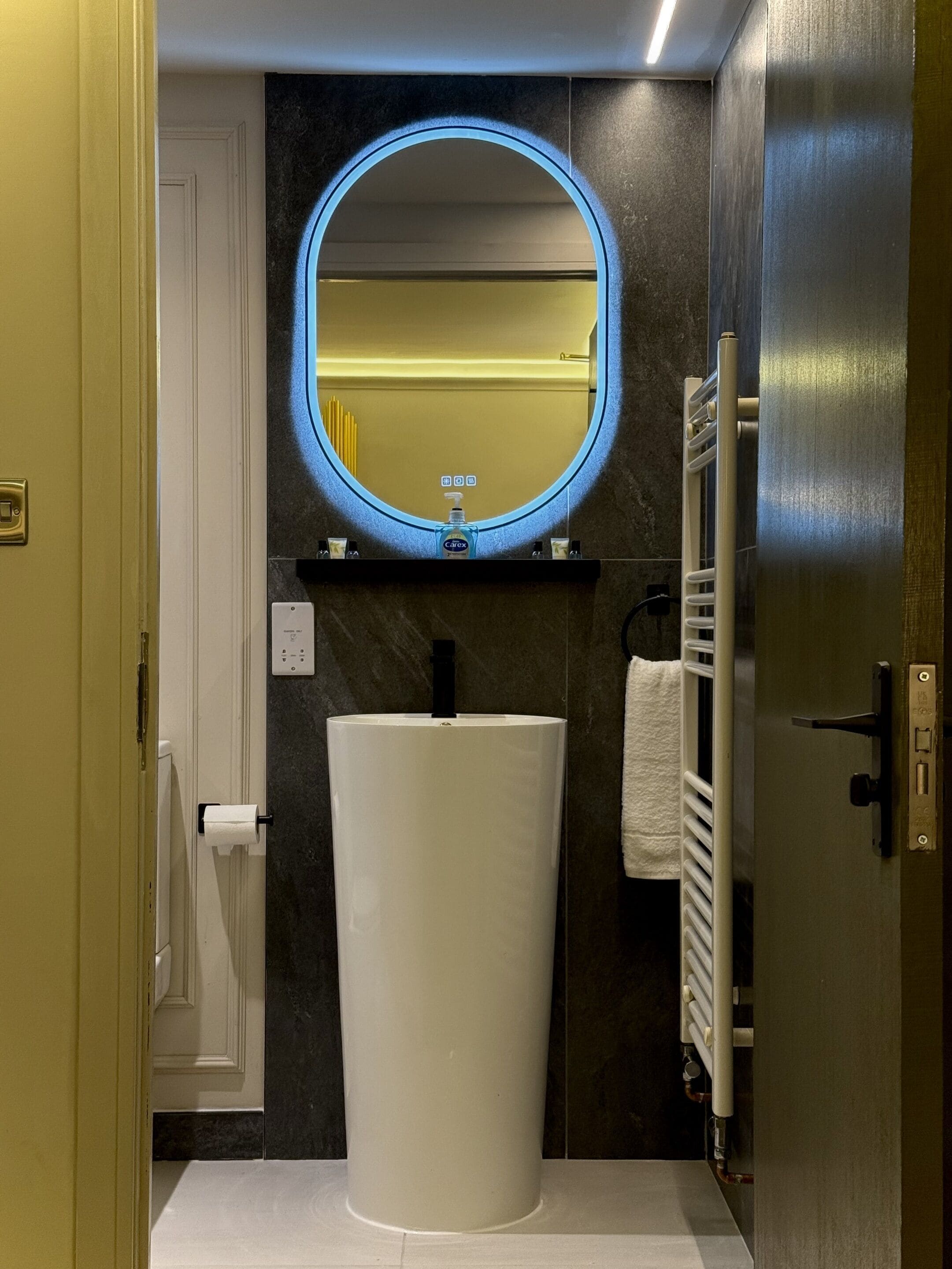 A bathroom with a white sink, a round mirror with a blue light, a towel rack, and a towel hanging on it.