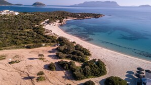 Eine Küstenlandschaft mit sandigem Strand, klarem blauen Meer und hügeligem Gelände mit Vegetation.