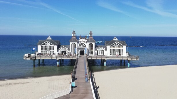 A pier leading to a white building with multiple windows and a central entrance, overlooking a beach and the ocean. - Jasmunder Inselglück vacation apartment for 4 people on Rügen - Jasmund (Sagard)