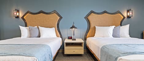 A hotel room with two beds, each with a headboard, a nightstand with a lamp, and a digital clock.