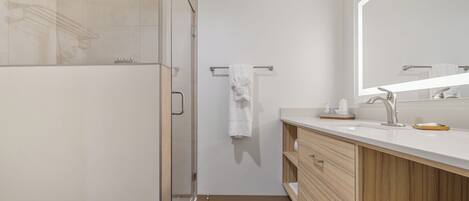 A modern bathroom with a glass shower enclosure, a wooden vanity, and a large mirror.